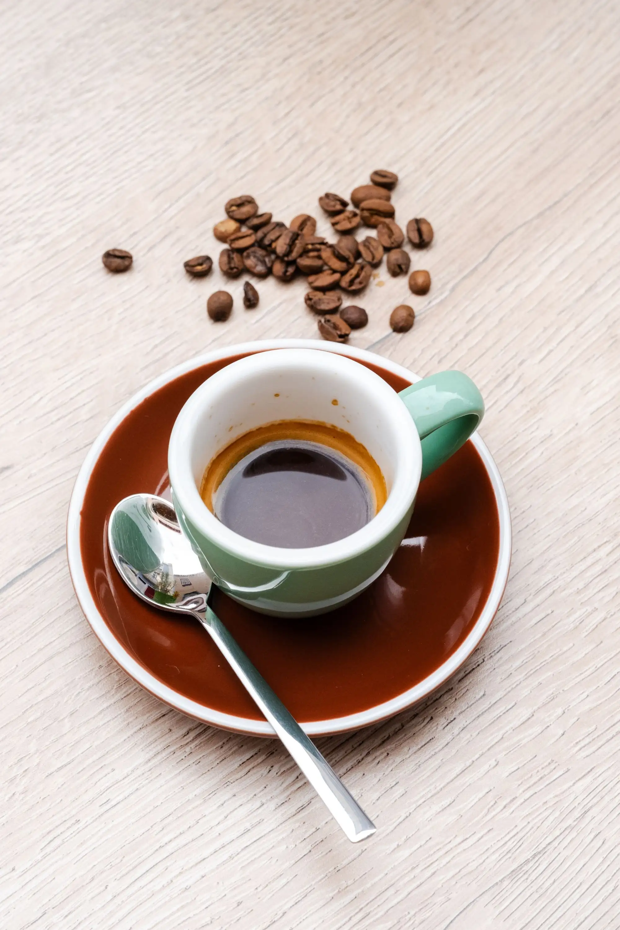 Espresso in a green cup on a brown saucer with scattered coffee beans