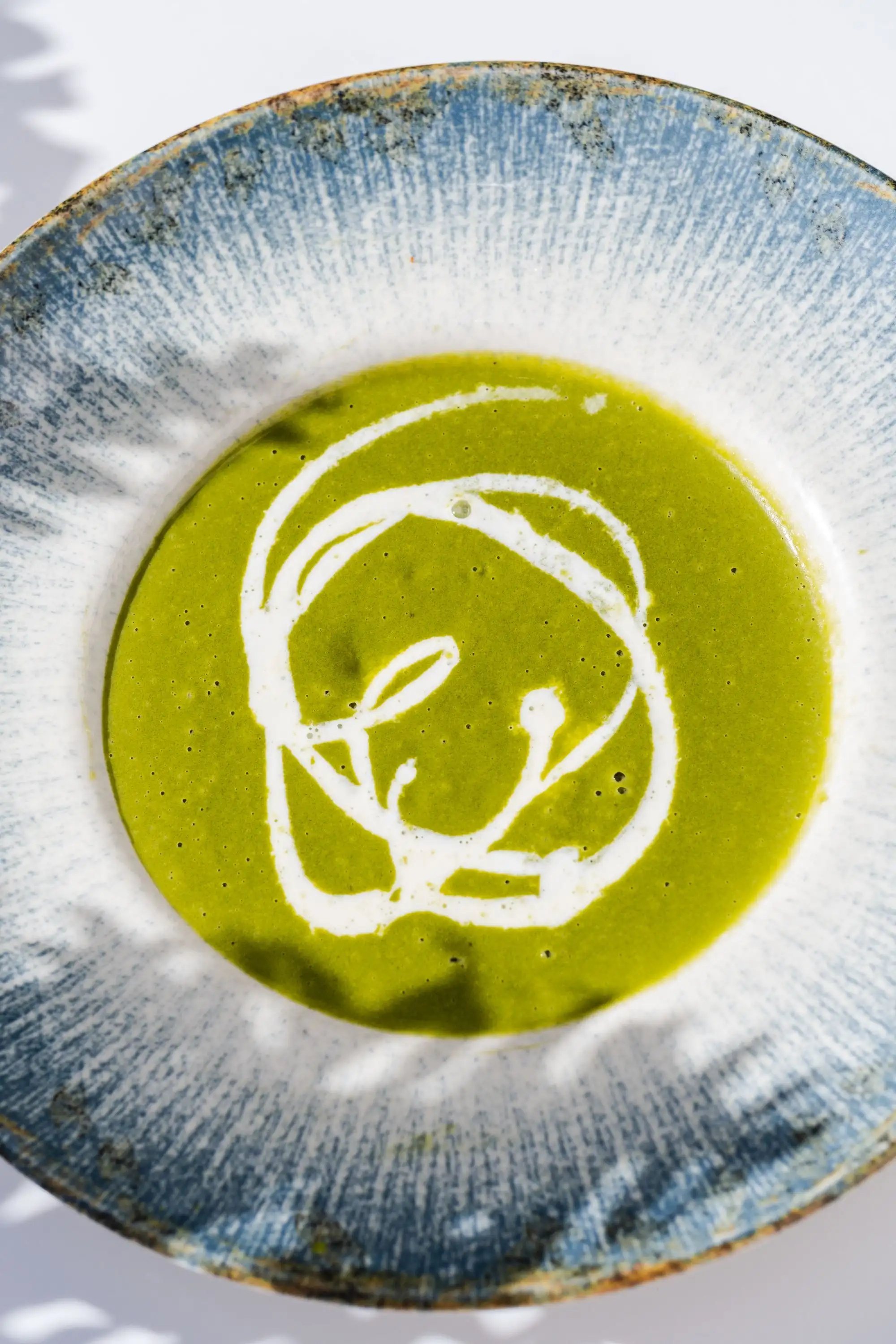 Green soup with a swirl of cream in a wide blue and white rimmed bowl