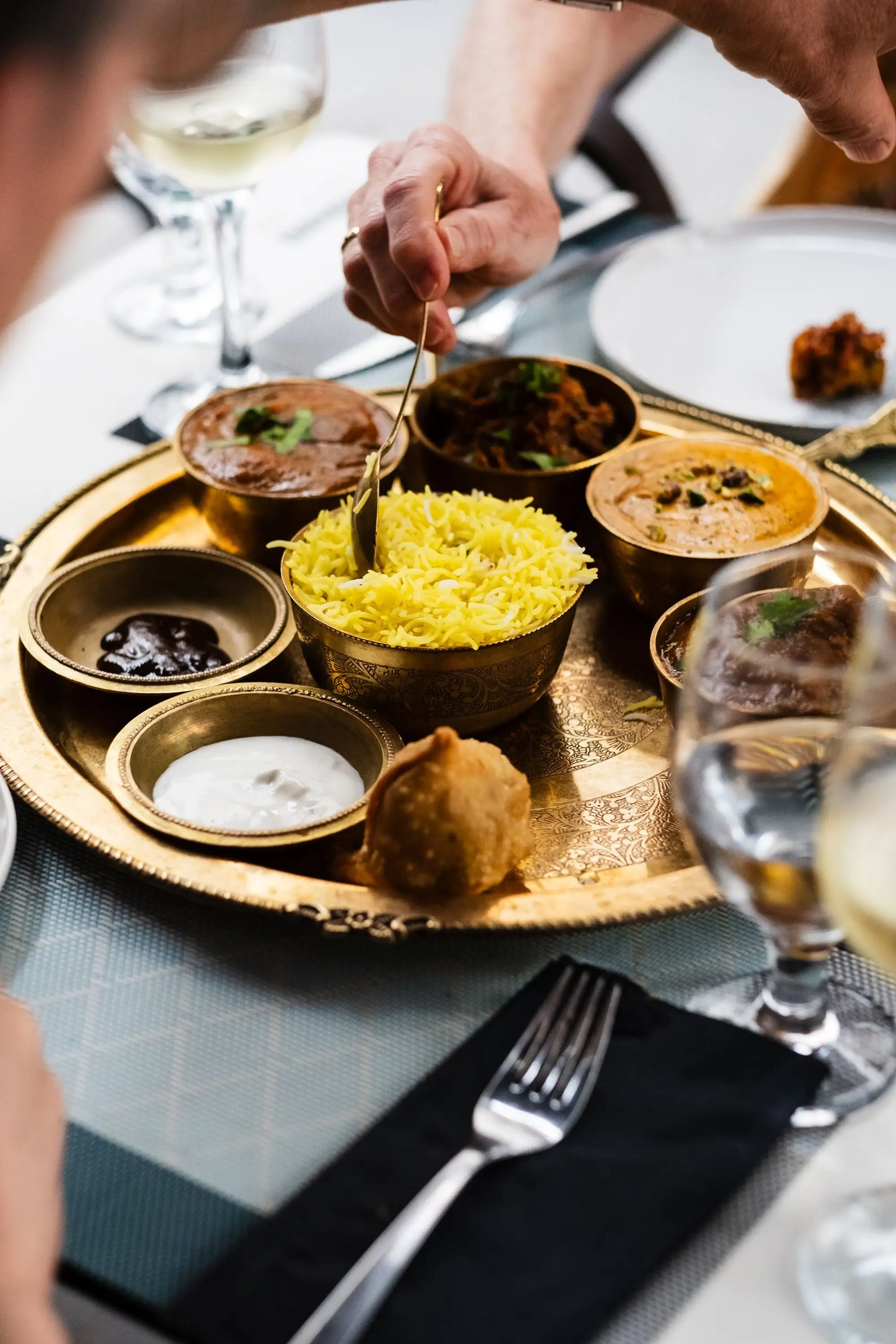 Brass tray with small bowls of curries, rice, samosa and chutneys on a restaurant table