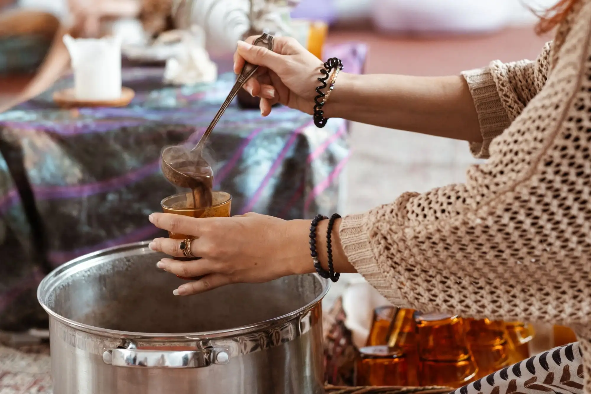 Hands ladling a hot chocolate drink from a large steel pot into a cup at a ceremony table