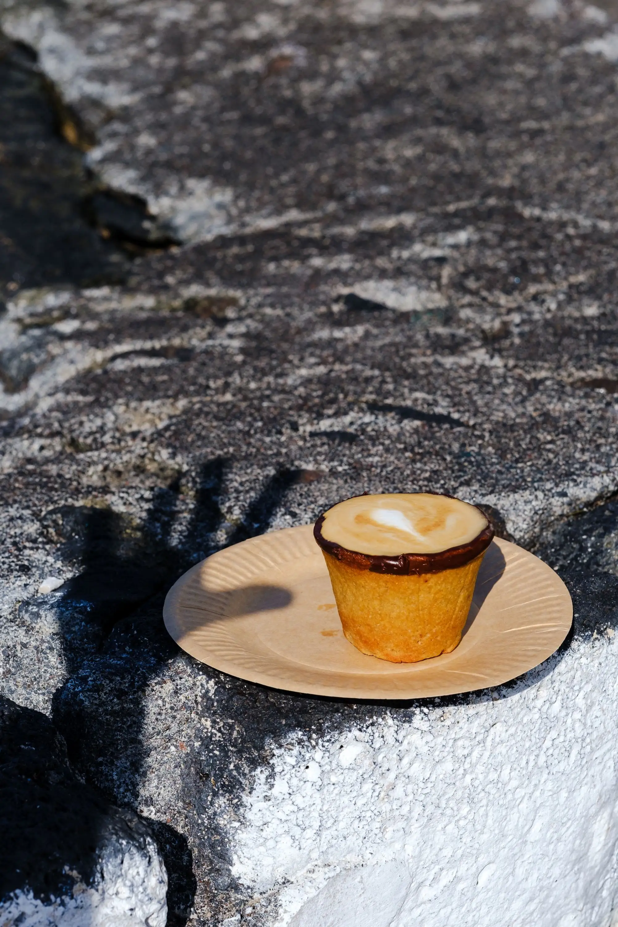 Latte served in an edible biscuit cup on a paper plate on a rough stone ledge