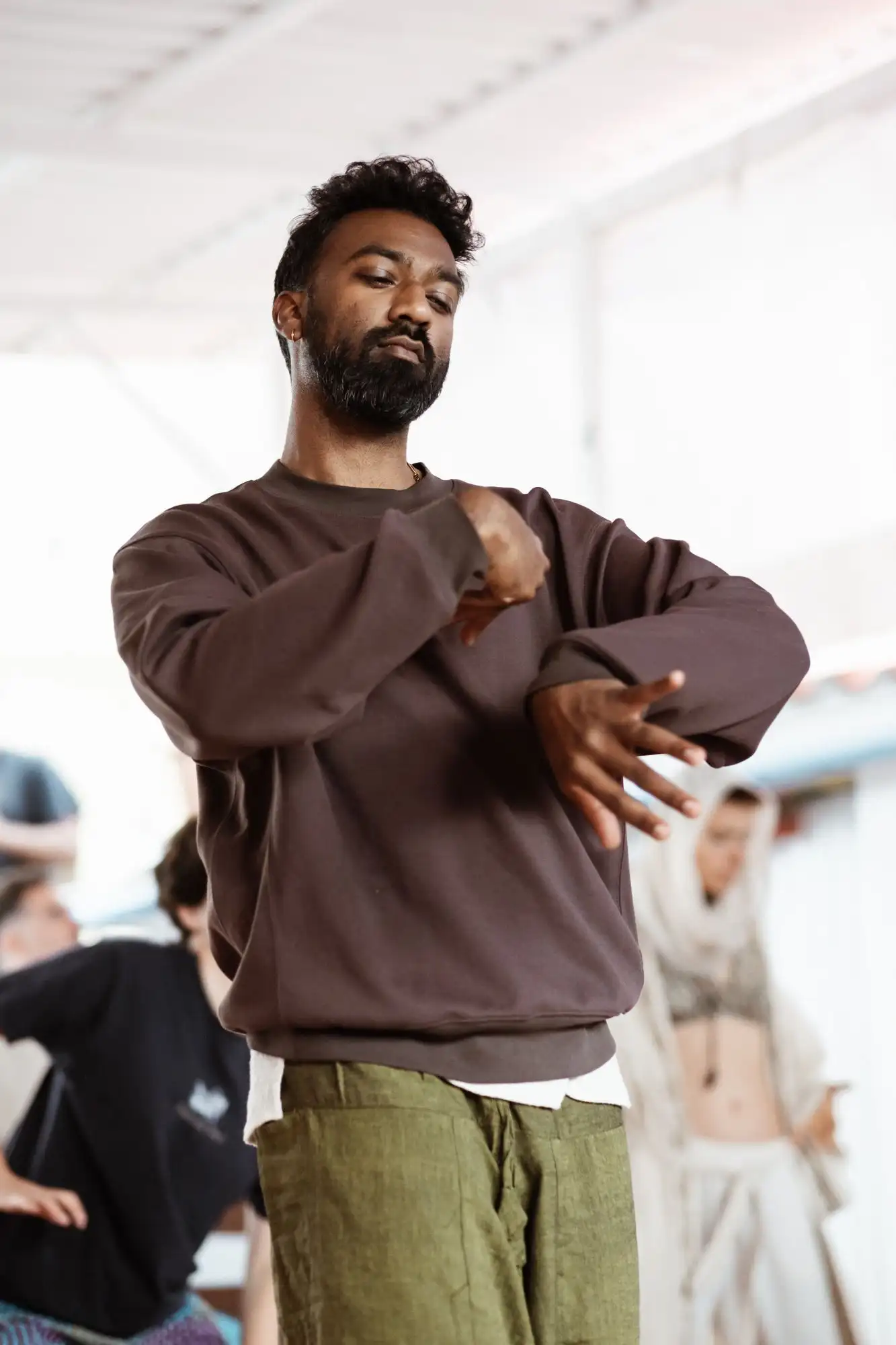 Bearded man in a brown sweatshirt moving his arms during an expressive dance session on a terrace