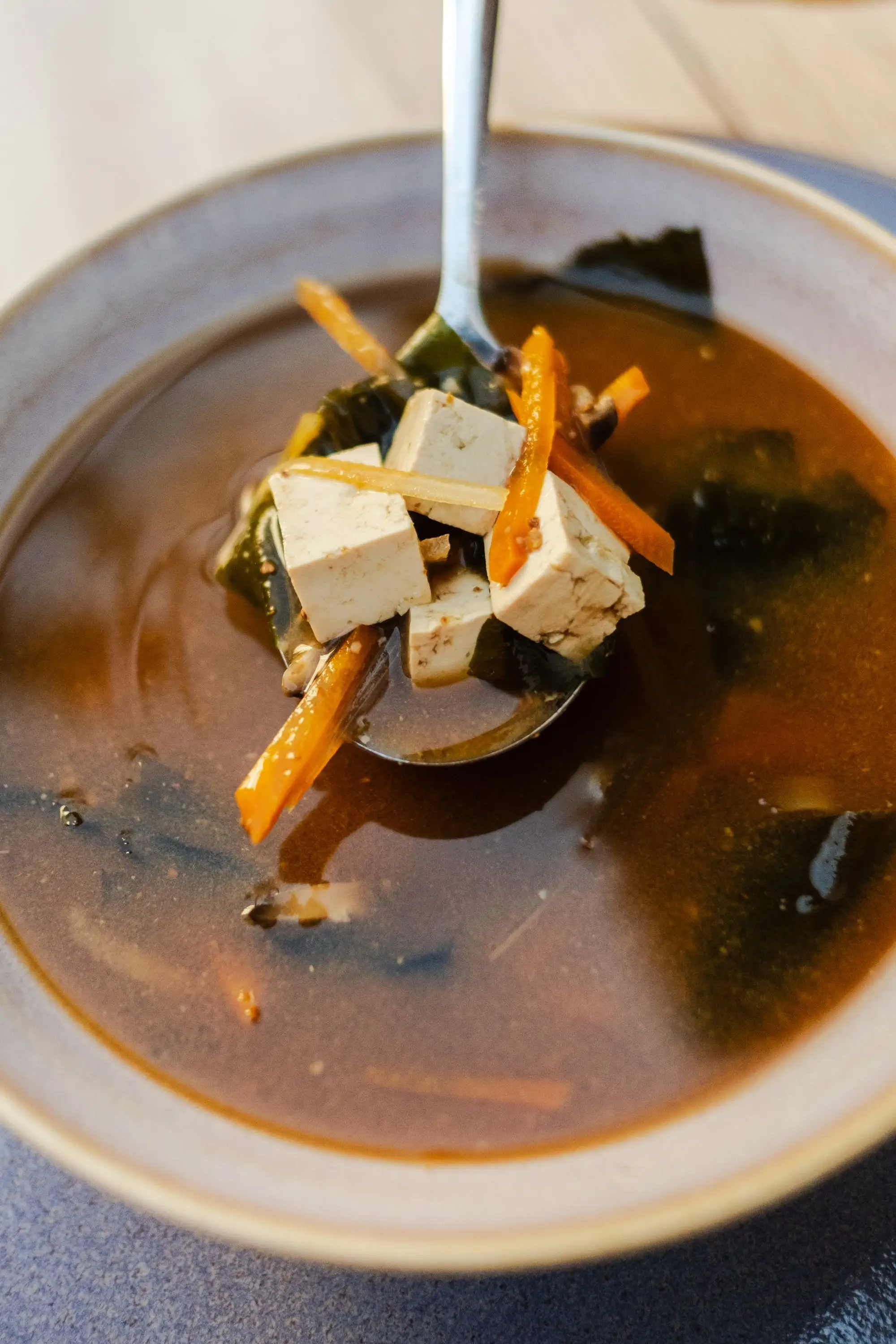 Spoonful of tofu, carrot and seaweed lifted from a bowl of dark miso soup