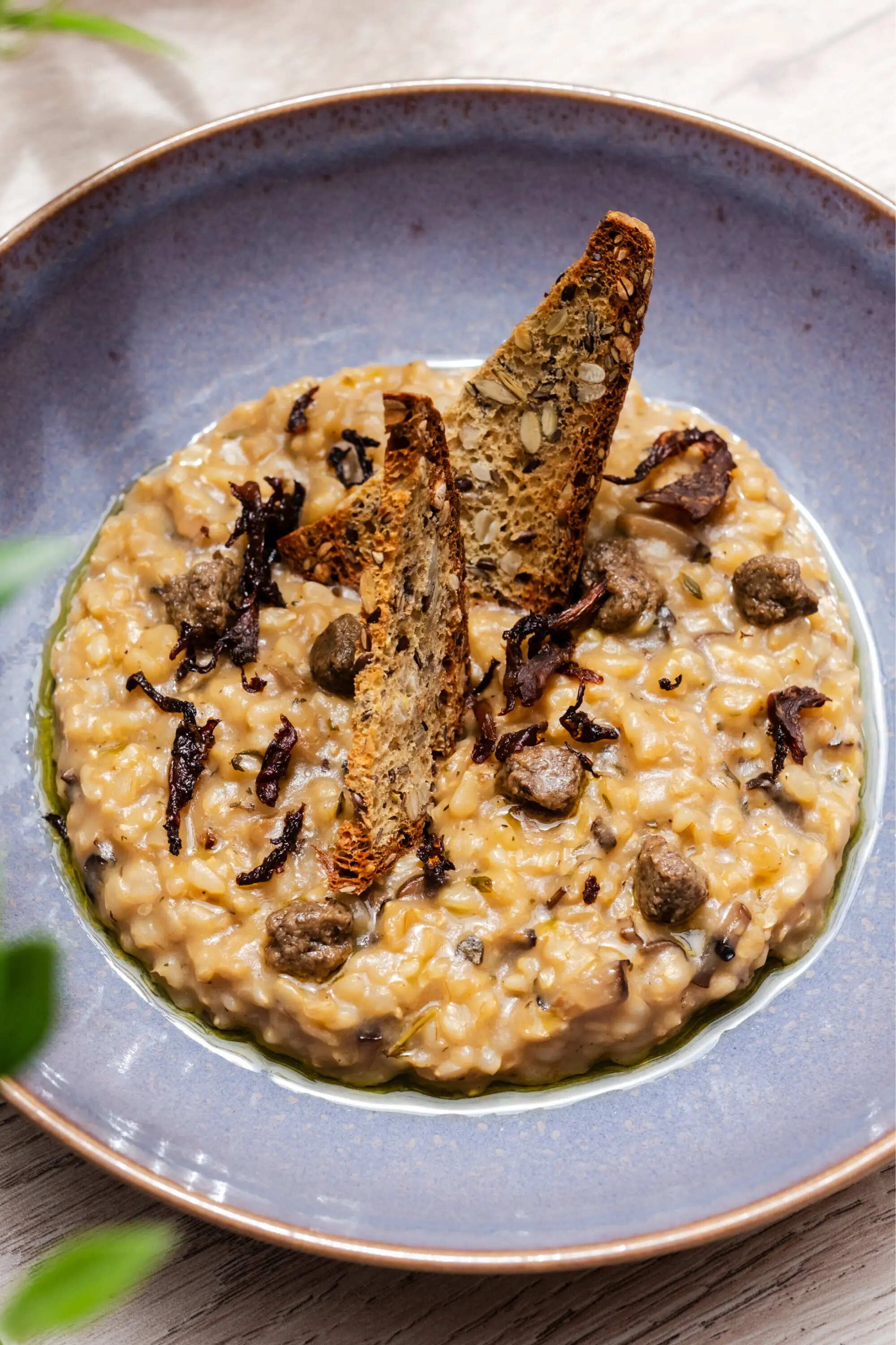 Mushroom risotto topped with slices of seeded toast in a blue bowl