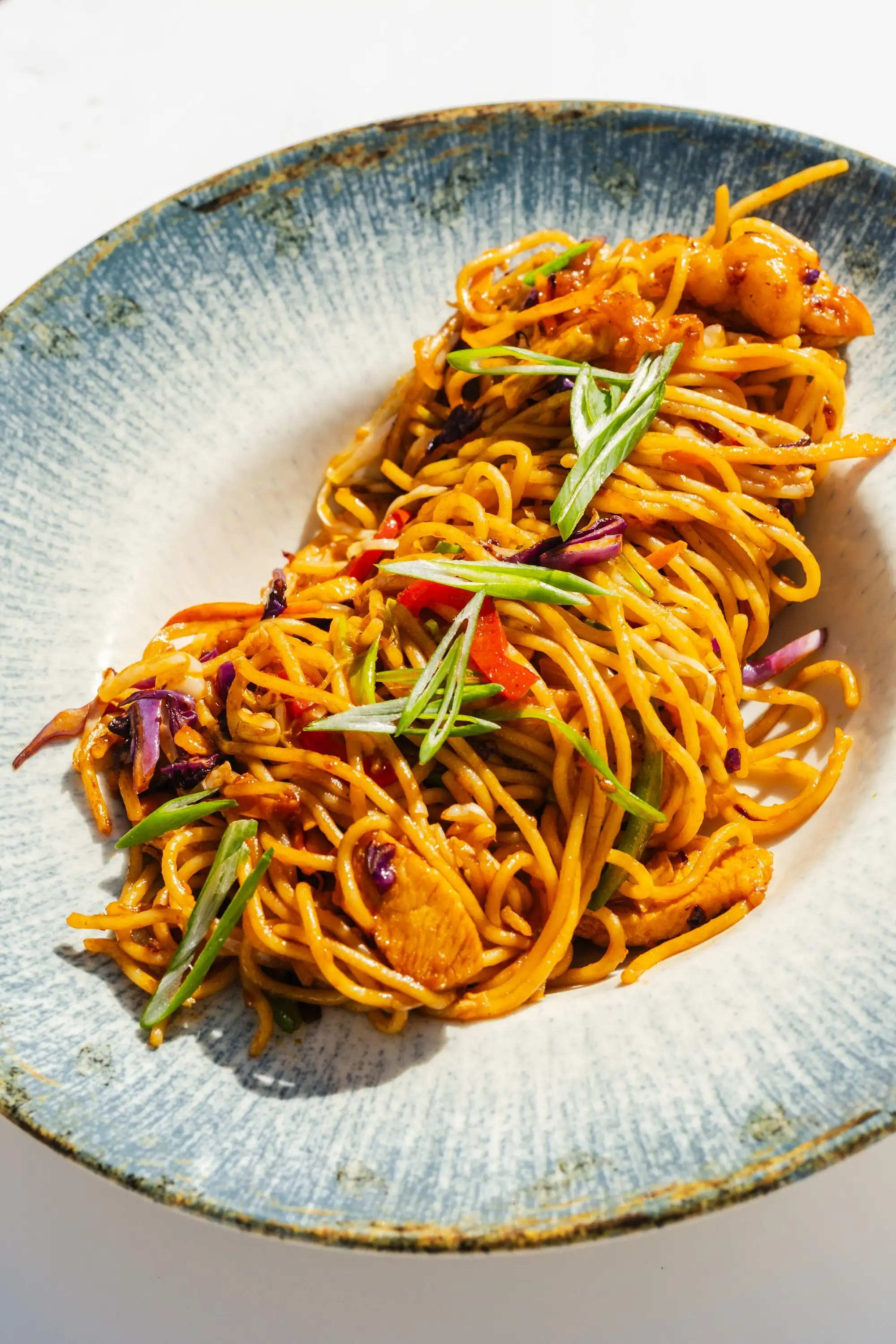 Stir-fried noodles with spring onion on a blue and white rimmed plate