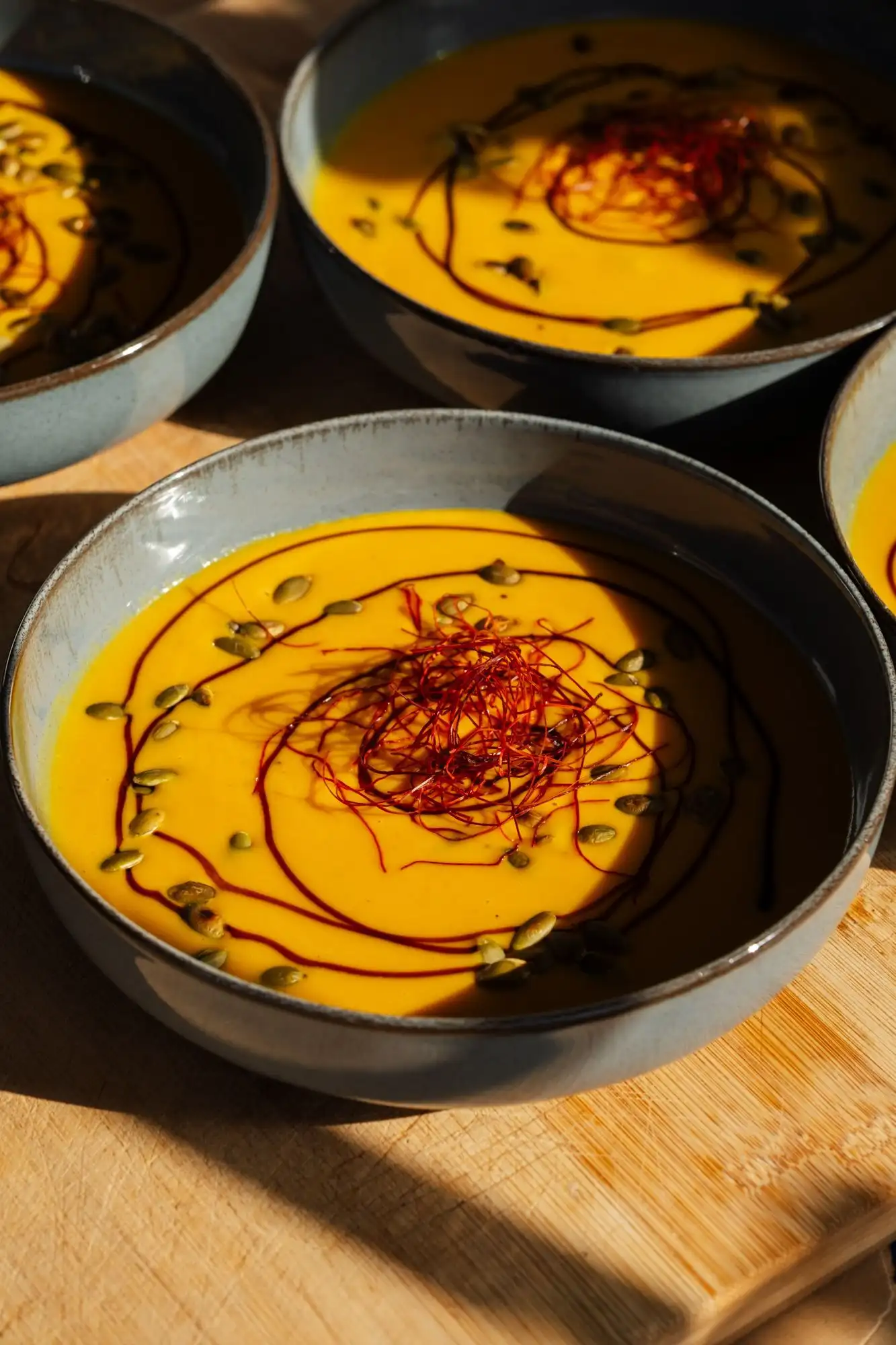 Bowls of orange pumpkin soup topped with chilli threads and pumpkin seeds on a wooden board
