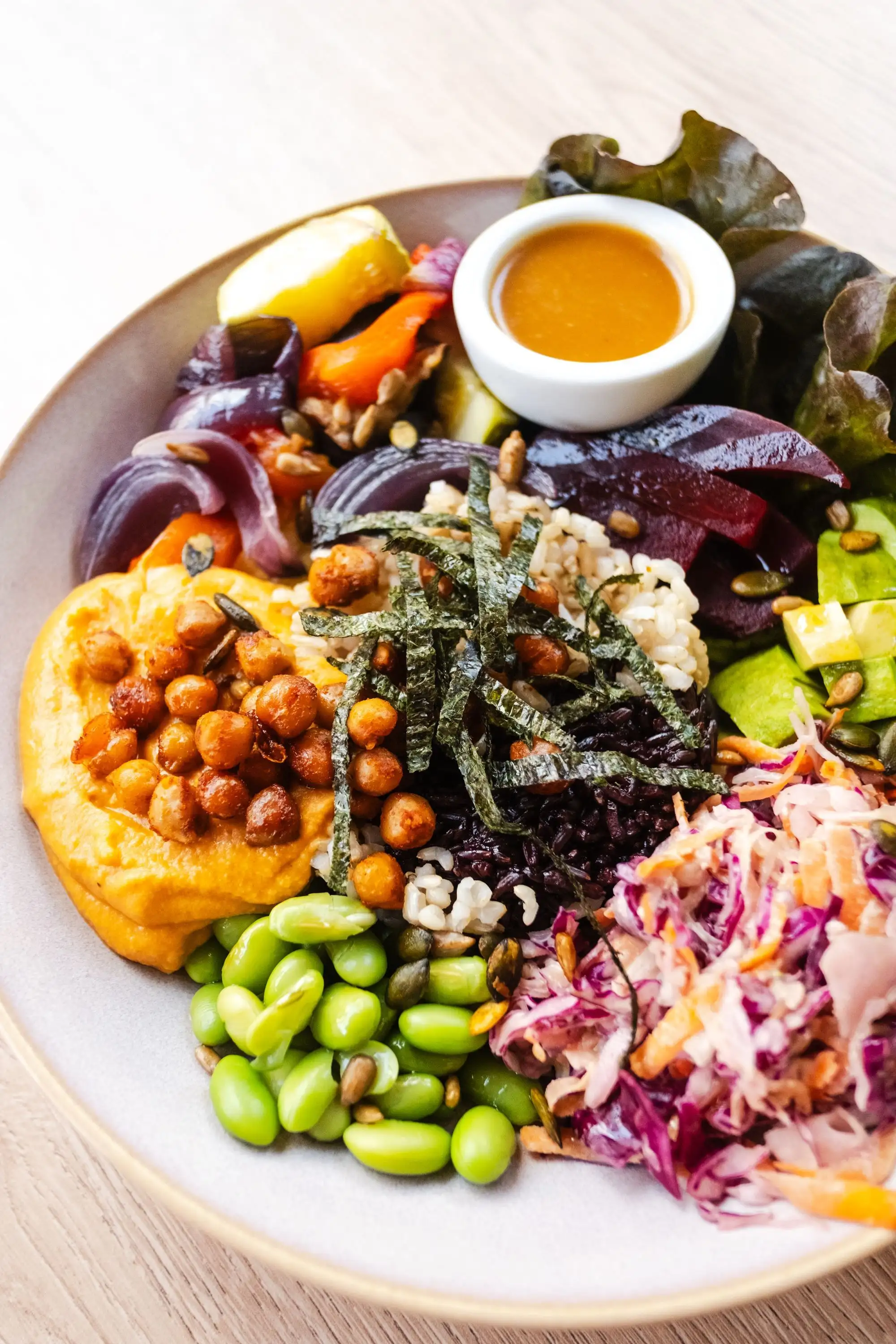 Colourful bowl with hummus, roasted chickpeas, edamame, red cabbage slaw and seaweed