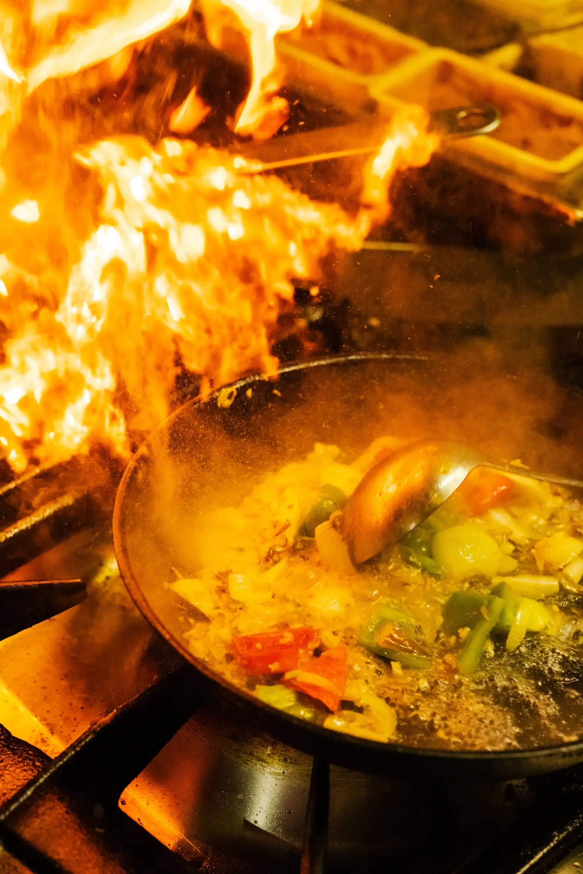 Flames rising from a pan of stir-fried vegetables on a gas stove