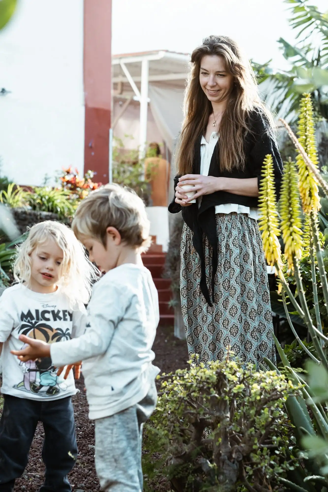 Woman with a cup standing in a garden with two young children near yellow aloe flowers