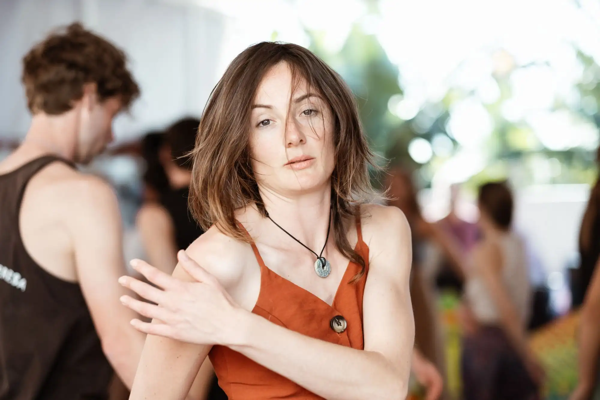 Woman with a bob haircut looking at the camera while a group moves around her in a bright room
