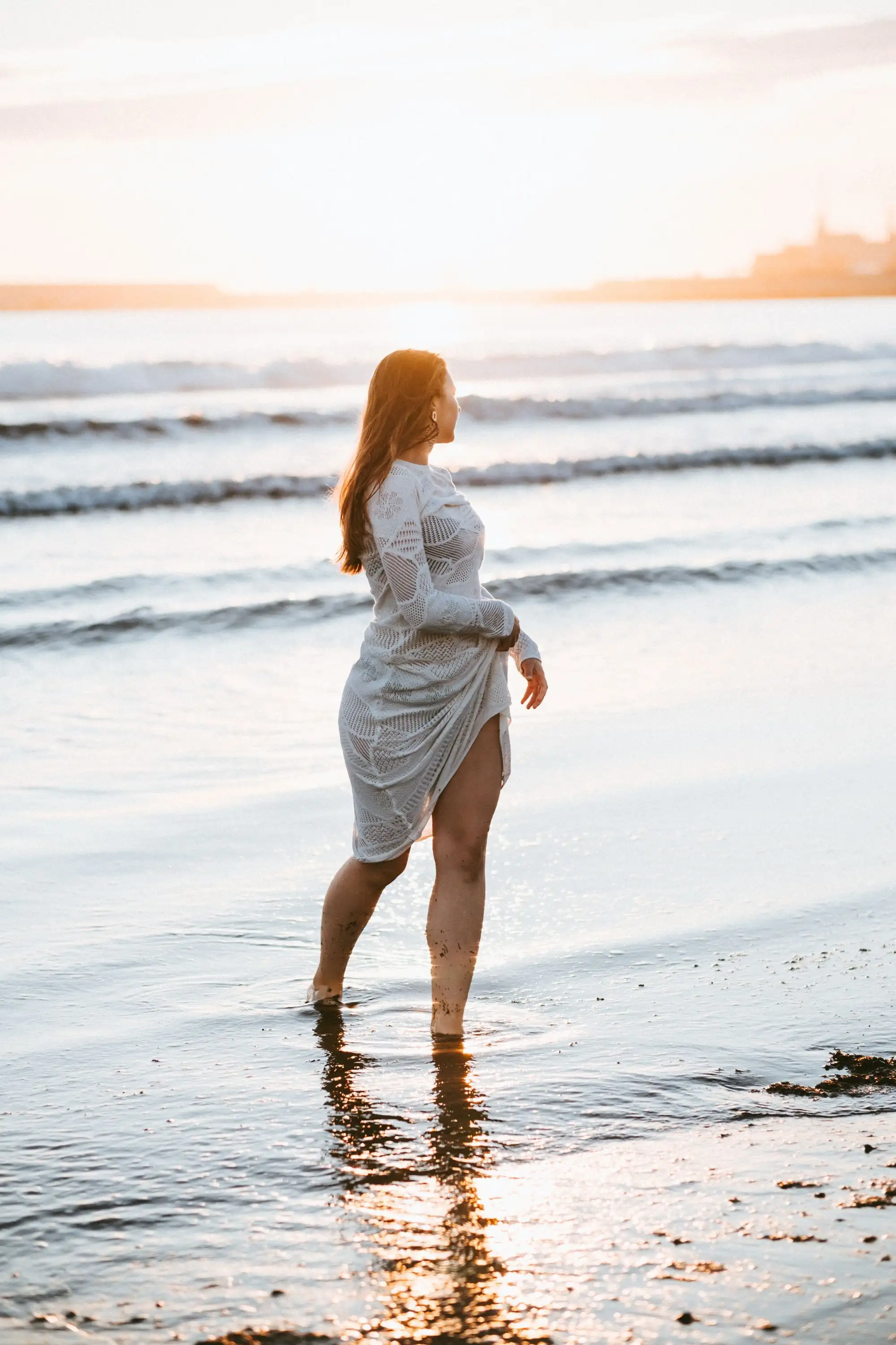 Woman in a white dress standing in the shallow water at sunset